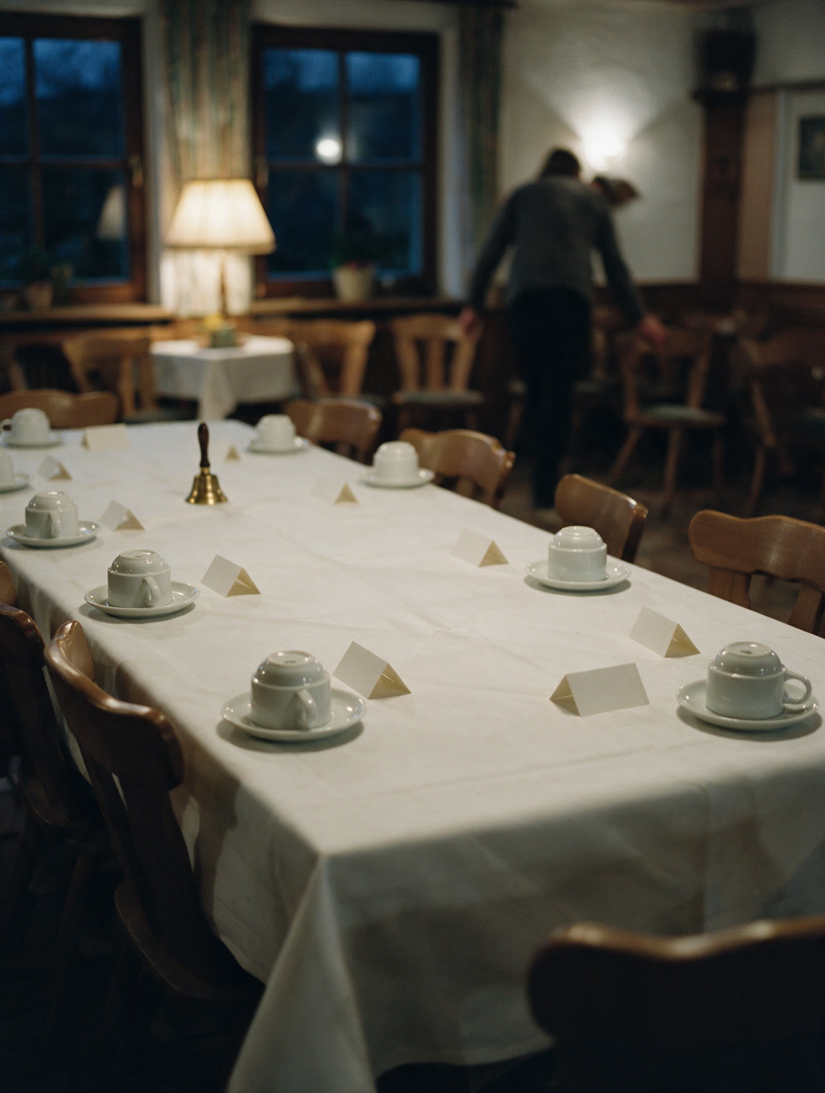 Gedeckter Frühstückstisch im Nebenraum eines Gasthauses: umgedrehte Kaffeetassen, leere Namenskarten, eine Messingglocke.
